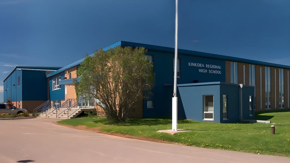Das moderne Schulgebäude der Kinkora Regional High School mit einer grünen Wiese und einem gepflasterten Weg im Vordergrund unter blauem Himmel.