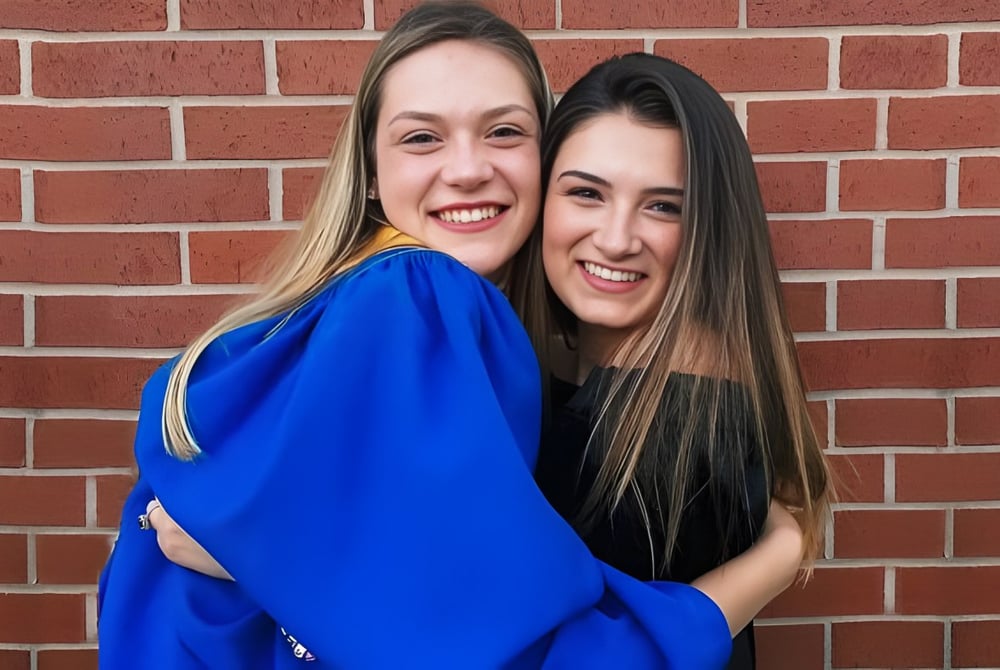 Zwei Schülerinnen der Kinkora Regional High School umarmen sich vor einer Backsteinwand.