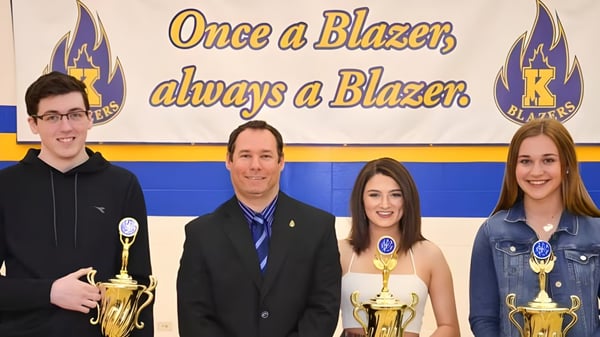 Vier Schüler der Kinkora Regional High School posieren vor einem Banner mit Trophäen.