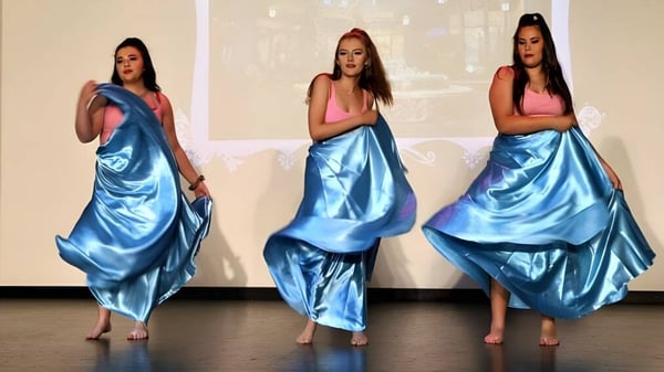 Drei Schülerinnen des Kinross College tragen lange blaue Satinkleider in einem Raum mit weißem Hintergrund.