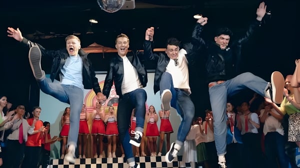 Eine Gruppe von Schülerinnen und Schülern der Kinsale Community School steht auf einer Bühne mit Schachbrettmuster und dekoriertem Hintergrund.