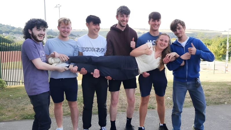 Eine Gruppe Schüler steht im Freien auf einer Wiese hinter einem Zaun auf dem Gelände der Kinsale Community School.