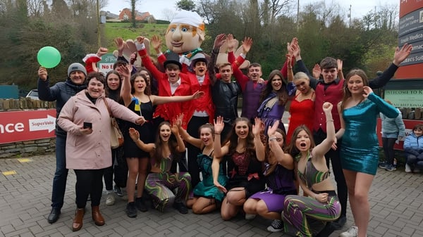 Eine Gruppe von Schülerinnen der Kinsale Community School posiert draußen vor Bäumen und Gebäuden in farbenfrohen Festkleidern.