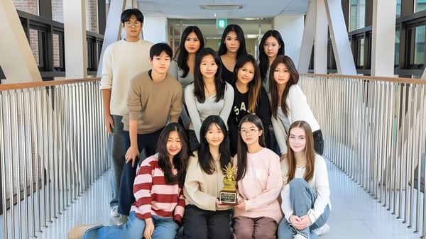 Eine Gruppe junger Schülerinnen steht gemeinsam im Flur der Korea International School mit einem Geländer im Hintergrund.