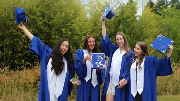 Vier Schülerinnen der Kitsilano Secondary School feiern ihren Abschluss in blauen Talaren im Wald.
