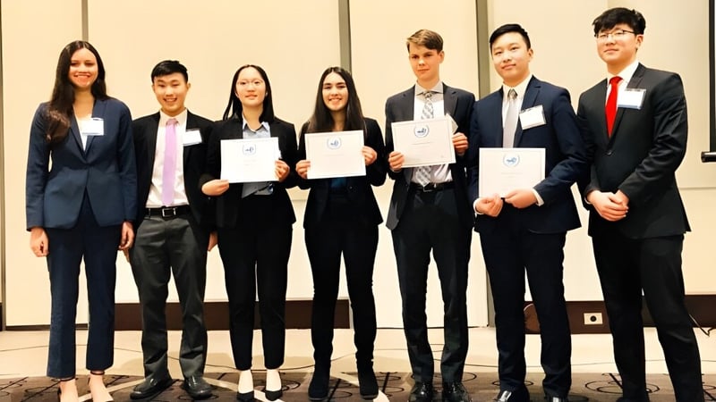 Schüler der Kitsilano Secondary School stehen in formeller Kleidung mit Zertifikaten vor neutralem Hintergrund.