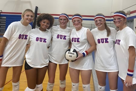 Eine Gruppe Schülerinnen der Kokomo Center Township Consolidated School Corporation steht in weißen Sportuniformen in der Turnhalle zusammen.