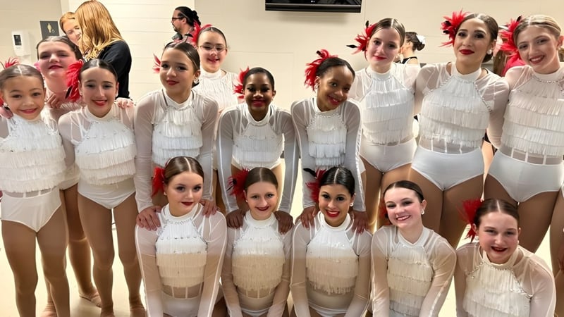 Eine Gruppe junger Tänzerinnen posiert gemeinsam in weißen und beigen Kostümen im Tanzstudio der Kokomo Center Township Consolidated School Corporation.