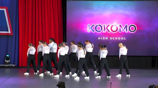 Schüler der Kokomo High School treten auf einer Bühne mit einem großen Schulnamen im Hintergrund auf.