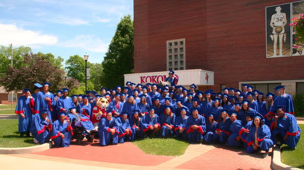 Absolventinnen und Absolventen der Kokomo High School stehen in blauen Talaren vor einem Backsteingebäude im Freien.