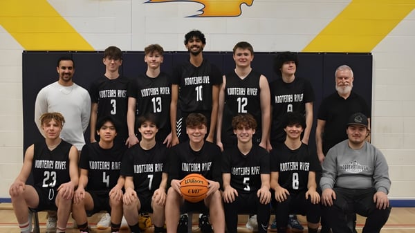 Die Basketballmannschaft der Kootenay River Secondary posiert gemeinsam in der Sporthalle vor einem großen gelb-schwarzen Logo.