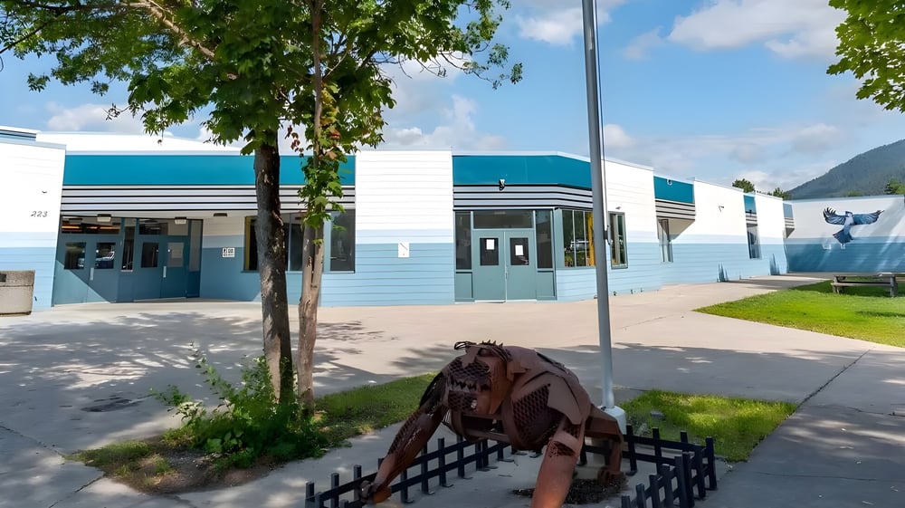 Eine Holzskulptur eines Pferdes steht auf dem Grün vor dem modernen Gebäude der Kootenay River Secondary.