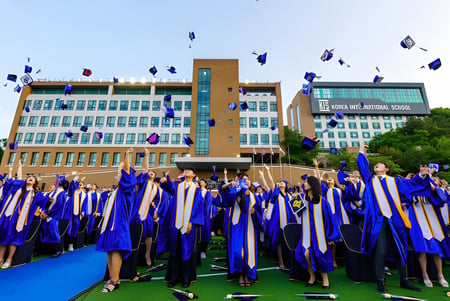 Absolventen der Korea International School werfen ihre Abschlussmützen vor dem Universitätsgebäude in die Luft.