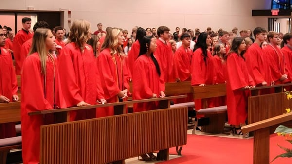 Schüler der Kuemper Catholic High School tragen rote Talare und sitzen in einer kirchenähnlichen Umgebung.
