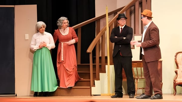 Schüler der Kuemper Catholic High School führen ein Theaterstück in historischen Kostümen auf einer Bühne mit Holztreppe auf.