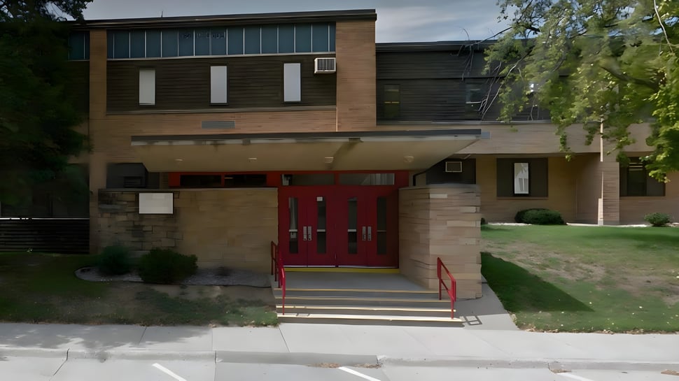 Das moderne mehrstöckige Gebäude der Kuemper Catholic High School mit rotem Eingang und Glasfenstern vor einer grünen Wiese.