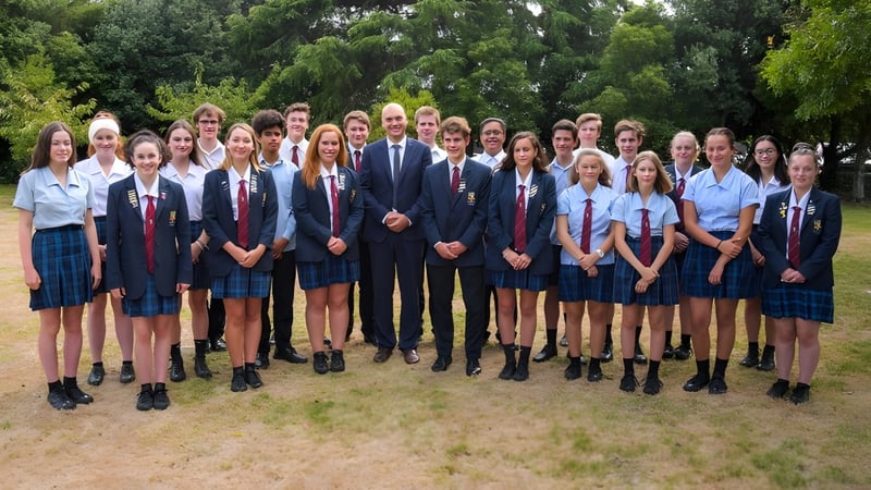 Schüler und Lehrkräfte posieren gemeinsam im Außenbereich des Kuranui College vor grüner Kulisse.