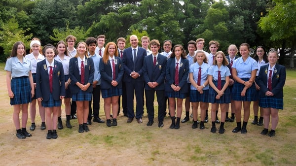 Schüler und Lehrkräfte posieren gemeinsam im Außenbereich des Kuranui College vor grüner Kulisse.