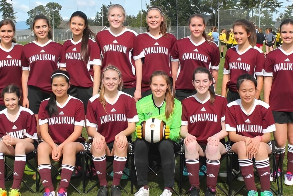 Eine Gruppe junger Fußballspielerinnen posiert auf dem Rasenfeld der Kwalikum Secondary School.