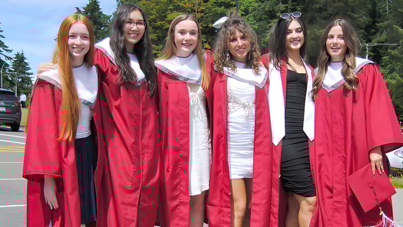 Eine Gruppe Schülerinnen der Kwalikum Secondary School steht in roten Abschlussroben vor einem bewaldeten Hintergrund.