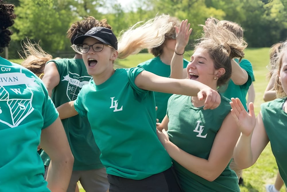 Eine Gruppe von Schülerinnen und Schülern der La Lumiere School feiert und jubelt im Freien vor grüner Kulisse.