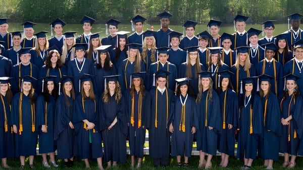 Absolventinnen und Absolventen der La Lumiere School stehen in akademischer Kleidung auf einer Wiese.