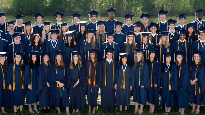 Absolventinnen und Absolventen der La Lumiere School stehen in akademischer Kleidung auf einer Wiese.