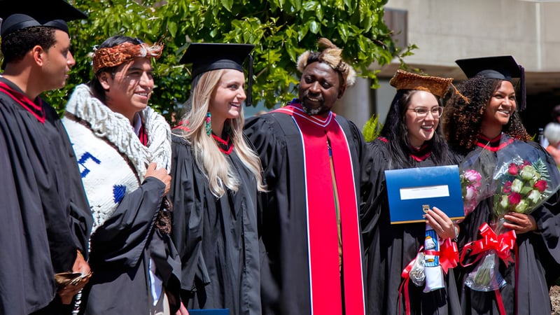 Eine Gruppe von Absolventinnen und Absolventen der La Salle Secondary School steht im Freien vor grüner Kulisse in akademischer Kleidung.