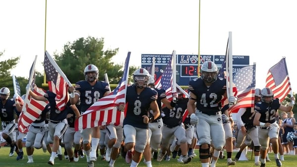 Eine Gruppe Football-Spieler läuft mit amerikanischen Flaggen auf das Spielfeld der Lacey Township High School.