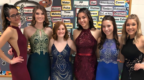 Eine Gruppe junger Frauen in formellen farbigen Kleidern posiert vor einer Wand mit musikalischen Begriffen auf dem Gelände der Lacey Township High School.