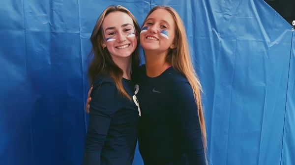 Zwei Schülerinnen der Lacey Township High School umarmen sich vor einem blauen Hintergrund und lächeln.