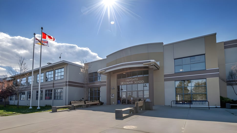 Das moderne mehrstöckige Gebäude der Ladysmith Secondary School mit gebogener Fassade und umgebenden Flaggen bei hellem Sonnenschein.