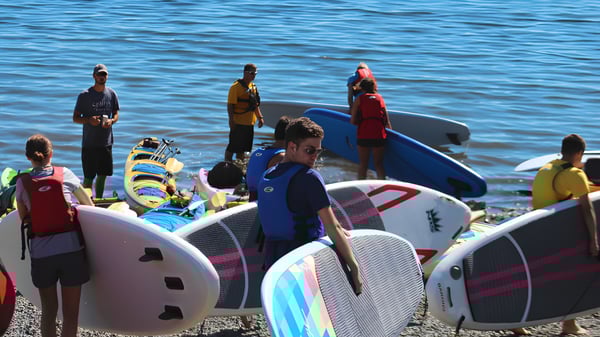 Schüler der Ladysmith Secondary School stehen auf Paddleboards auf einem Gewässer mit blauem Hintergrund.