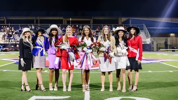 Eine Gruppe von Schülerinnen der Lafayette Christian Academy steht nachts auf dem Fußballfeld und hält Blumensträuße bei einer Feier.