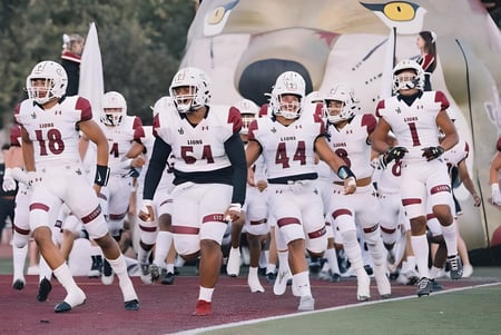 Eine Gruppe von Footballspielern in weißen Uniformen läuft auf das Spielfeld der Lafayette Christian Academy zu.