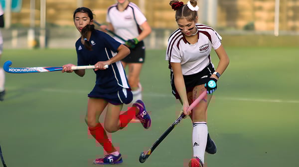Zwei Schülerinnen der Lake Cowichan Secondary School spielen auf einem Sportplatz ein Feldhockeyspiel.