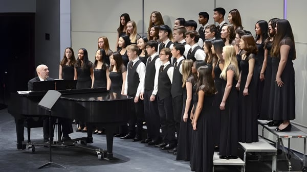 Ein großer Chor steht in formeller schwarzer Kleidung auf der Bühne der Lake Forest Academy mit einem Flügel im Vordergrund.