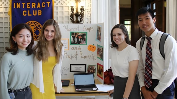 Vier Schüler stehen vor dem Interact Club Infobrett auf dem Campus der Lake Forest Academy.