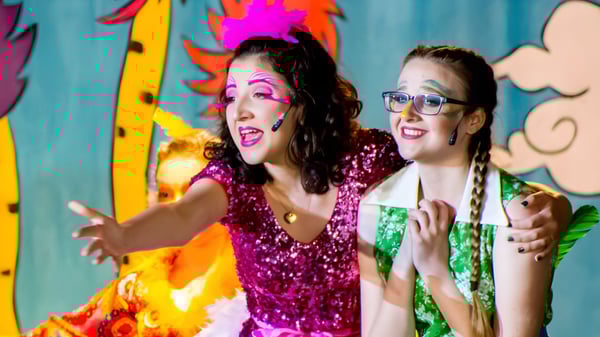 Zwei Frauen in bunten, glitzernden Outfits vor einem farbenfrohen, abstrakten Hintergrund auf dem Campus der Lake Mary Preparatory School.