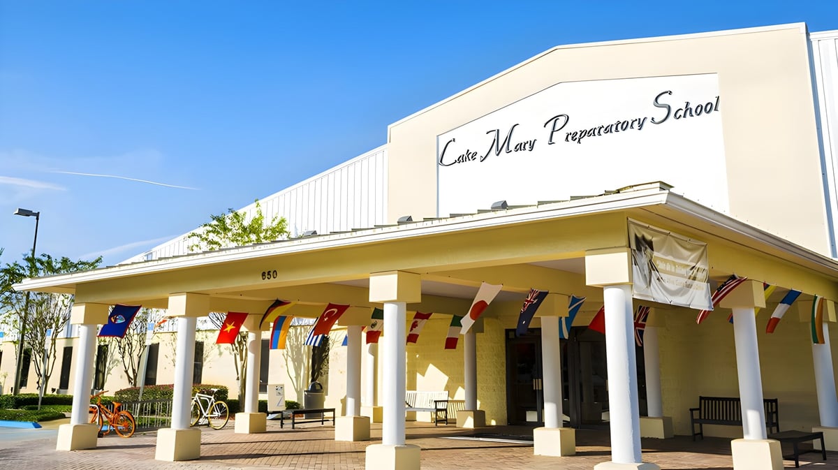 Das große gelbe Schulgebäude der Lake Mary Preparatory School mit überdachtem Eingang und wehenden Flaggen.