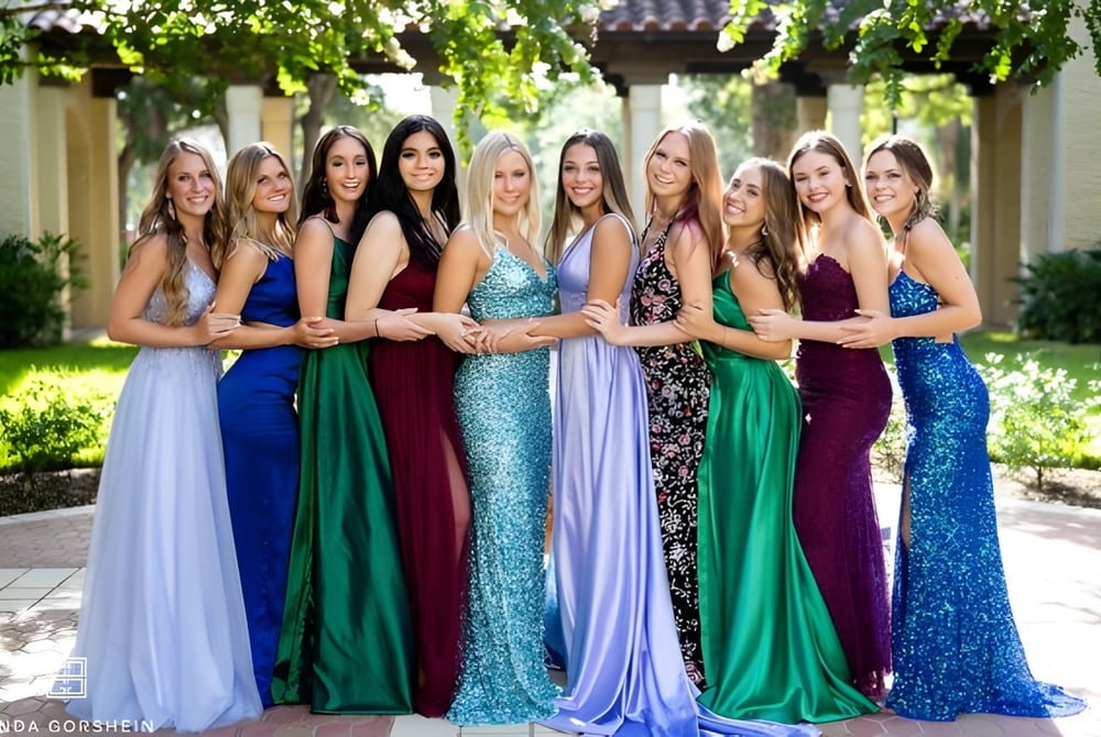 Eine Gruppe Schülerinnen der Lake Mary Preparatory School steht in farbenfrohen Kleidern zusammen in einem Garten mit Bäumen und Architektur.