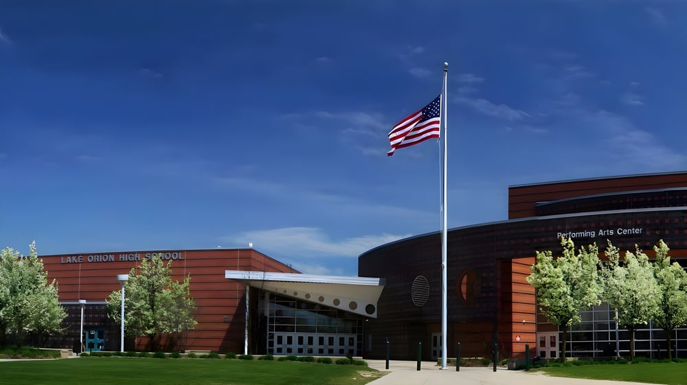 Das moderne Schulgebäude der Lake Orion High School mit amerikanischer Flagge und Bäumen auf dem Schulgelände.