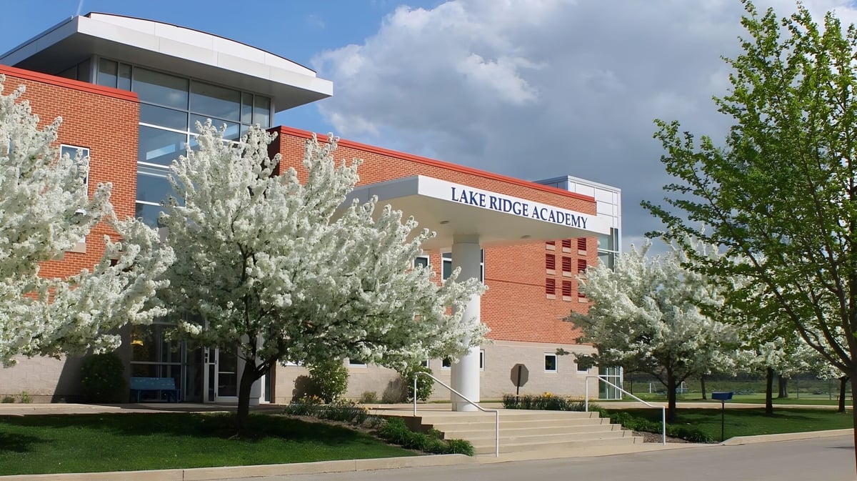 Das Backsteingebäude der Lake Ridge Academy ist umgeben von blühenden Bäumen und einem Rasen unter bewölktem Himmel.