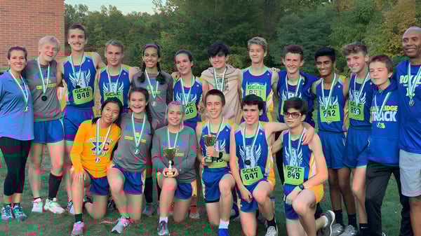 Eine Gruppe von jungen Athleten trainiert auf dem Sportplatz der Lake Ridge Academy mit Bäumen und einem Backsteingebäude im Hintergrund.