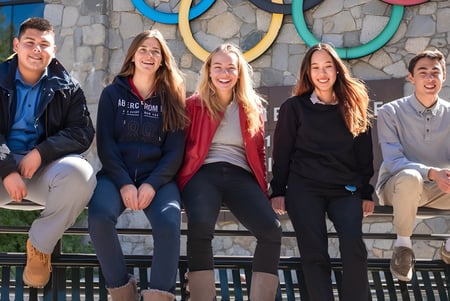 Fünf Schülerinnen und Schüler der Lake Tahoe Preparatory School sitzen auf einer Holzbank vor einer Wand mit bunten kreisförmigen Mustern.