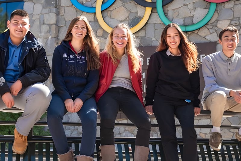 Fünf Schülerinnen und Schüler der Lake Tahoe Preparatory School sitzen auf einer Holzbank vor einer Wand mit bunten kreisförmigen Mustern.