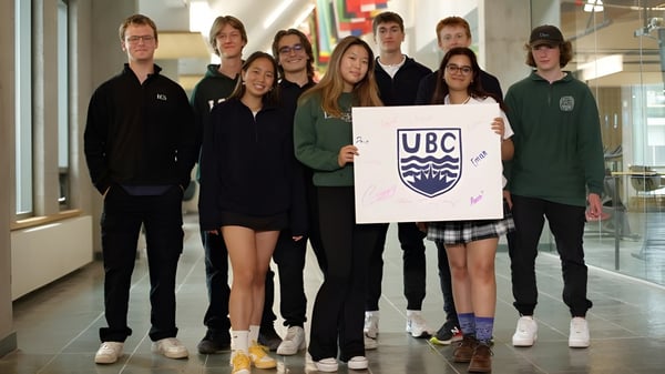 Eine Gruppe Schüler der Lakefield College School steht zusammen in einem Schulgebäude und hält ein Schild mit dem UBC-Logo.