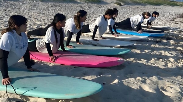 Eine Gruppe von Schülerinnen und Schülern der Lakeland Senior High School steht in Neoprenanzügen am Strand mit bunten Surfbrettern.