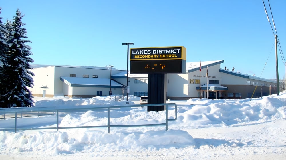 Der verschneite Campus der Lakes District Secondary School zeigt ein großes Schild vor blauem Himmel.