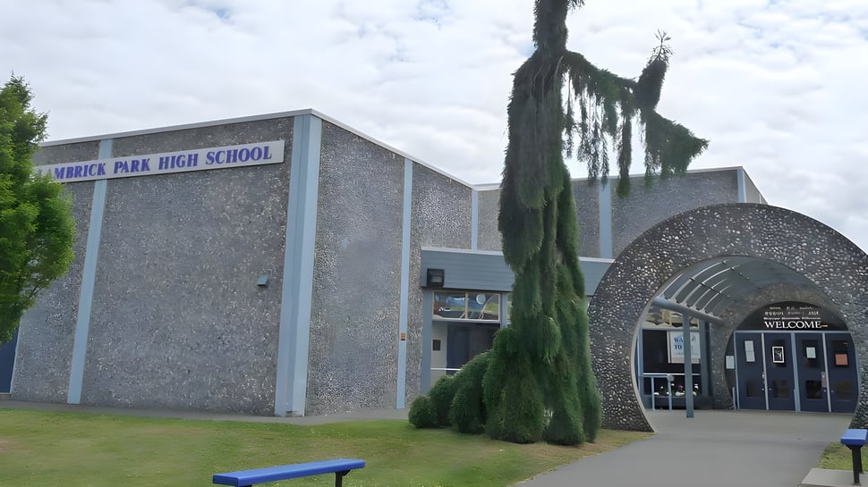 Das moderne Gebäude der Lambrick Park Secondary School mit einer schlanken Zypresse im Vordergrund vor bewölktem Himmel.